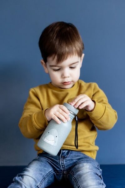 Child holding a Trixie 350ml stainless steel water bottle with a friendly shark face design