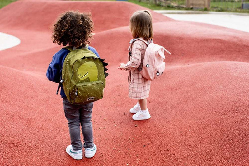 Children wearing cute backpacks, including green Backpack - Mr. Dino, at playground with red surface