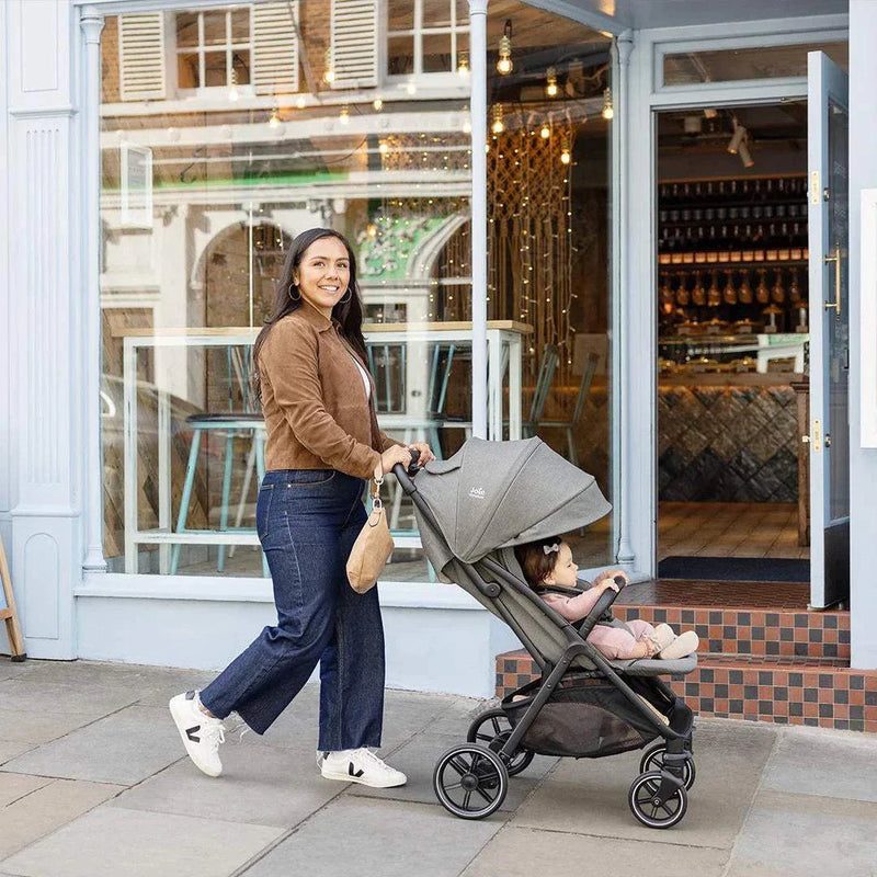Woman pushing a child in a gray Joie Parcel LX Signature Stroller outside a cafe