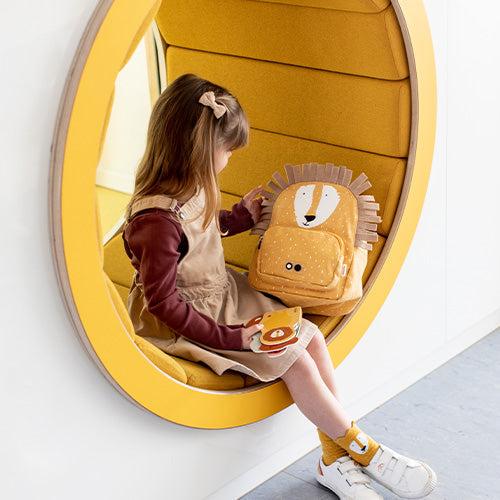 Child sitting in yellow seat holding Trixie Backpack Mr. Lion with lion face design